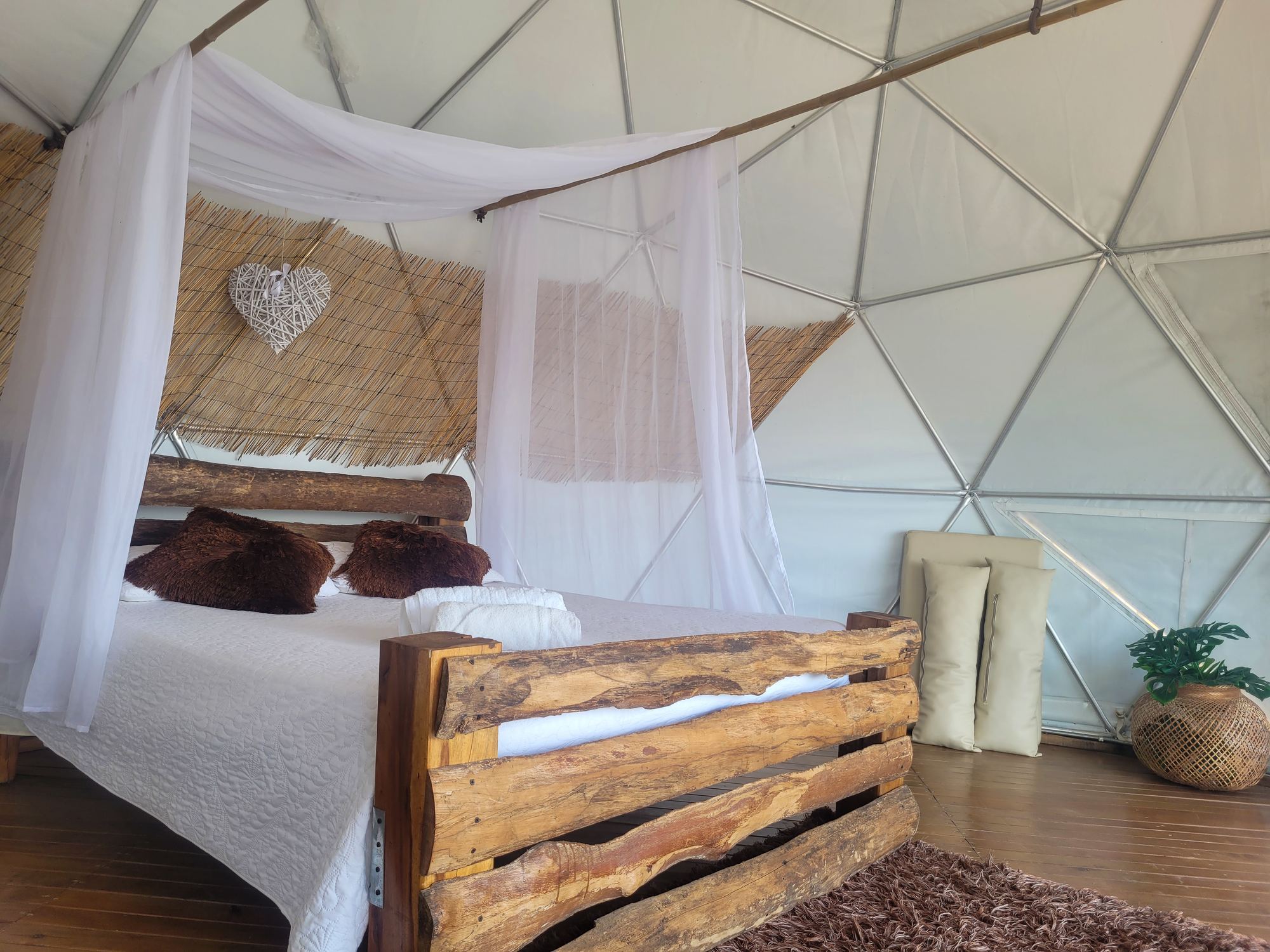 Glamping dome interior with a rustic wooden bed and white canopy