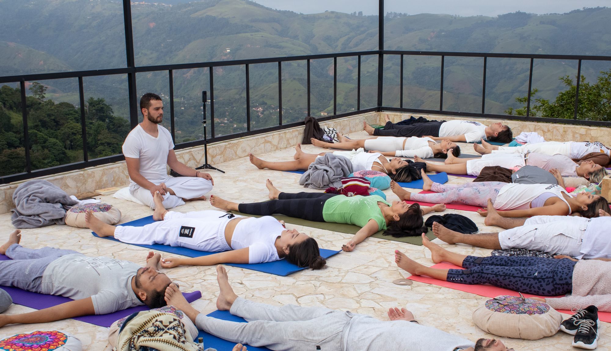 Wellness retreat guests resting on mats on a rooftop above the mountains
